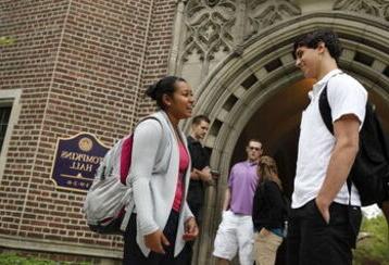 A male and female student talk and laugh near an entrance to Tompkins Hall as other students talk in the background